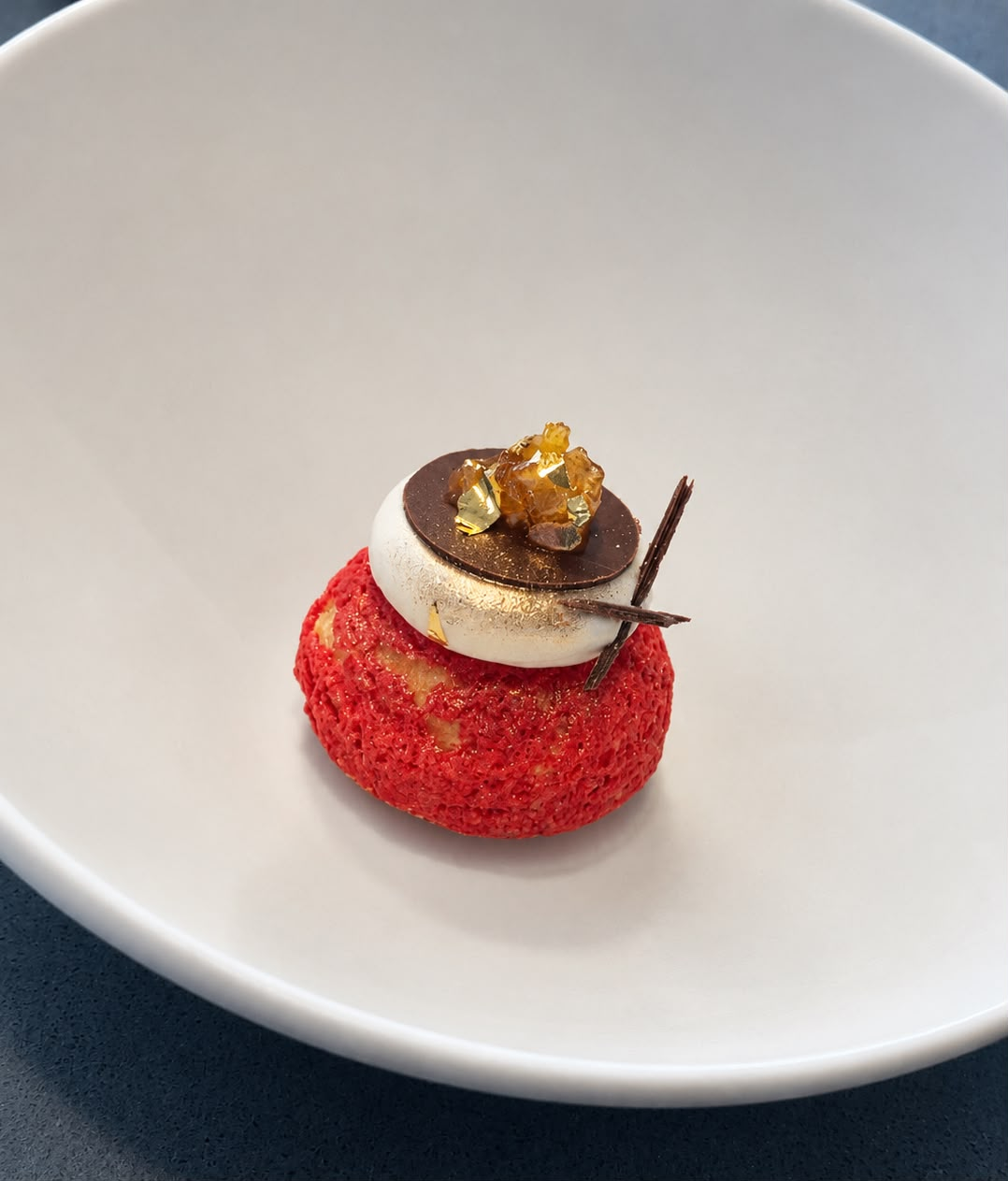 Chef Diego Alejandro's individual creation with a red pastry, cream, chocolate and gold decoration on a white plate